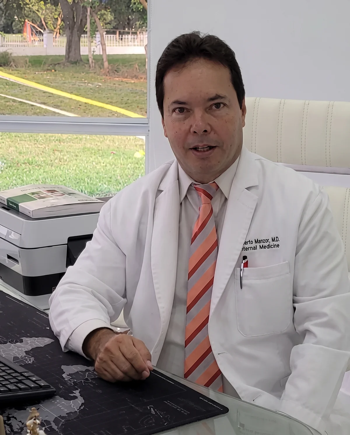 Dr. Alberto Manzor in his white coat at his office desk